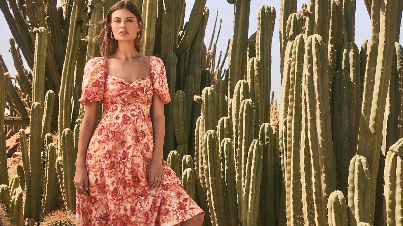 model standing in front of a bunch of tall cacti in a peach and coral floral dress with puff sleeves and cut out just under the bust