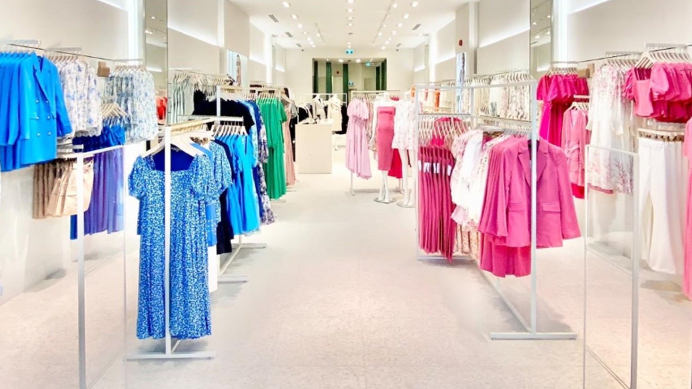 a shot of inside a brightly lit Ever New store, you can see all vibrant blue styles hung on racks on the left and all bright pink styles on racks displayed on the right side